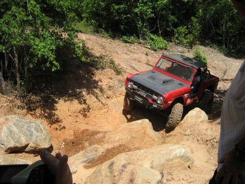 1995 Ford Bronco - This classic SUV navigates a challenging rocky terrain on a wooded trail.
