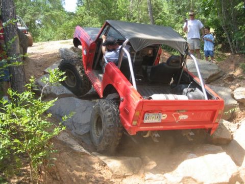 1995 Ford Bronco - This red off-road SUV is navigating a challenging rocky trail, with another vehicle visible in the background.