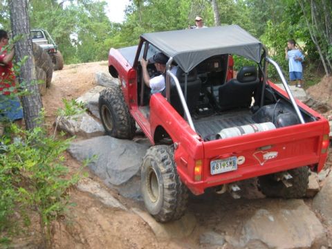 1995 Ford Bronco - A red Bronco is shown off-roading on a rocky trail with another vehicle in the background.