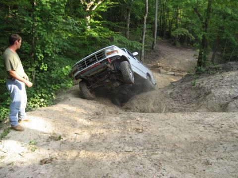 1995 Ford Bronco - A white SUV navigates a challenging off-road obstacle on a wooded trail.