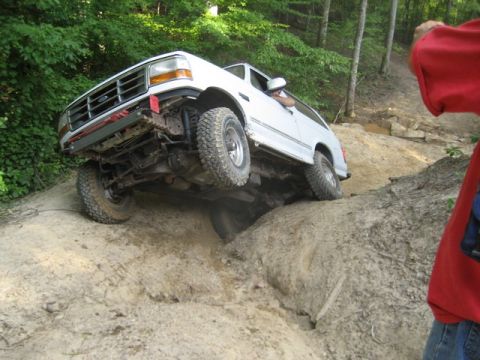 1995 Ford Bronco - A white 1995 Ford Bronco tackles a challenging off-road trail, with its front wheels high on a rocky ledge.