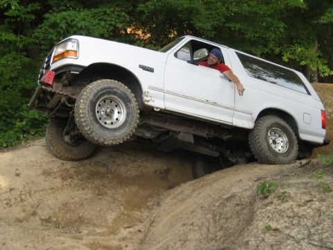 1995 Ford Bronco - 1995 Ford Bronco navigating a challenging off-road obstacle with its front tire lifted.