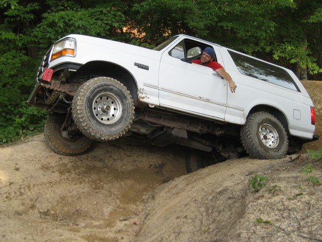 White 1995 Ford Bronco with lifted suspension driving on a dirt trail, front wheel off the ground