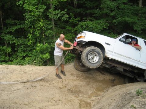 1995 Ford Bronco - A man is winching a white Ford Bronco out of a ditch while off-roading in a wooded area.