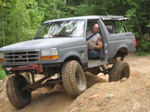 1995 Ford Bronco - This lifted 1995 Ford Bronco navigates a dirt trail with its driver visible.