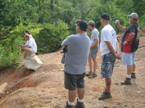 1995 Ford Bronco - Spectators observe an off-road event in a wooded area, with one person perched on a rock.