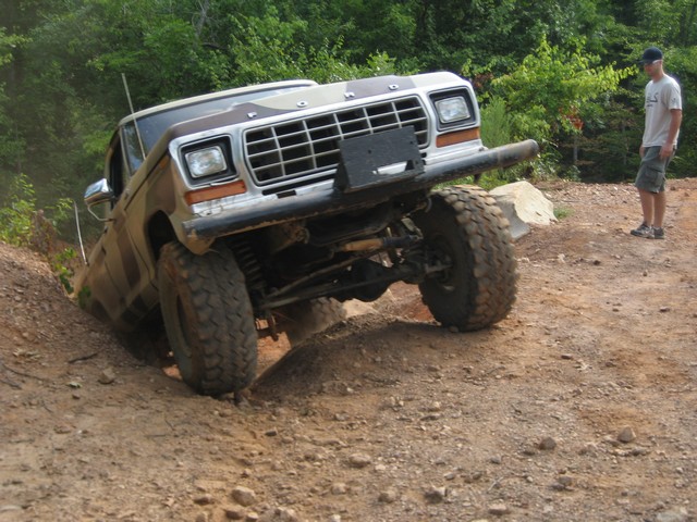 Brown and camouflage Ford F-Series truck on a dirt trail, front-left wheel in a ditch