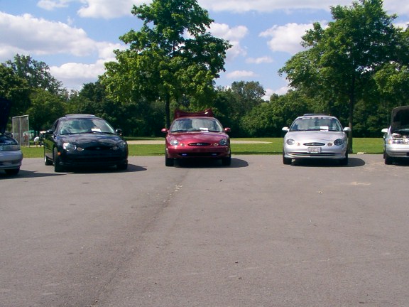 three Ford Tauruses parked in a lot, one black, one red, one silver