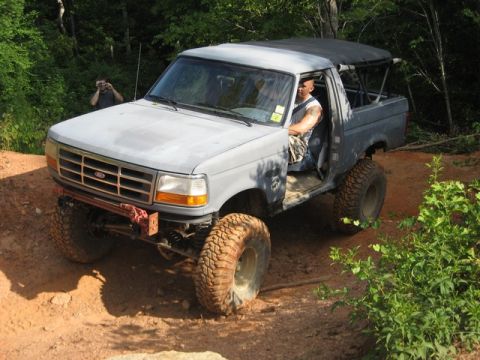 1995 Ford Bronco - A modified 1995 Ford Bronco navigates an off-road trail with its doors removed.