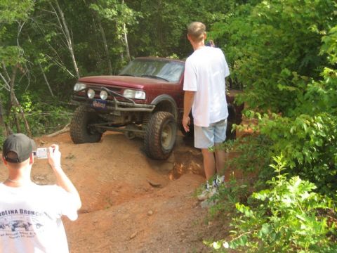 1995 Ford Bronco - A red SUV is captured mid-trail, equipped for off-road adventure with large tires and a protective brush guard.