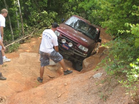 1995 Ford Bronco - A red SUV is stuck on a challenging off-road trail with people attempting to free it.
