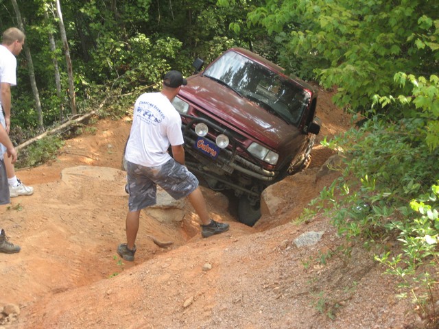 red SUV stuck on a dirt trail, people trying to push it out