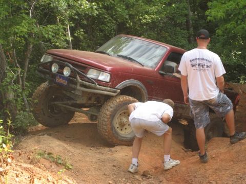 1995 Ford Bronco - This red SUV, identified as a 1995 model, navigates a challenging off-road trail with two people observing.
