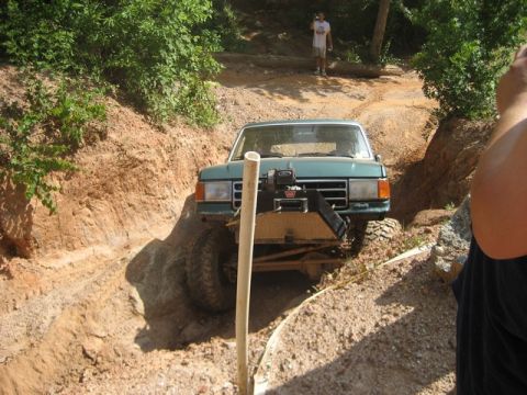 1995 Ford Bronco - A green 1987 Ford F-Series truck is shown navigating a challenging dirt trail, equipped with a winch for off-road recovery.