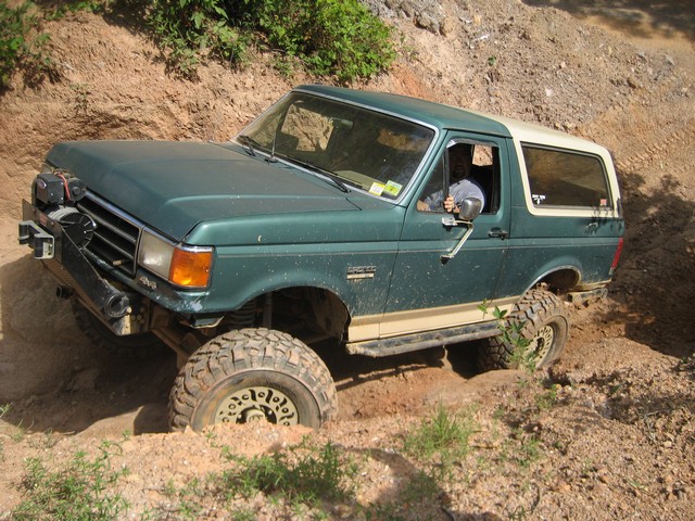 Green 1995 Ford Bronco with off-road tires navigating a dirt trail