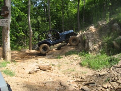 1995 Ford Bronco - A blue Jeep Wrangler navigates a challenging off-road trail with steep inclines and large rocks.