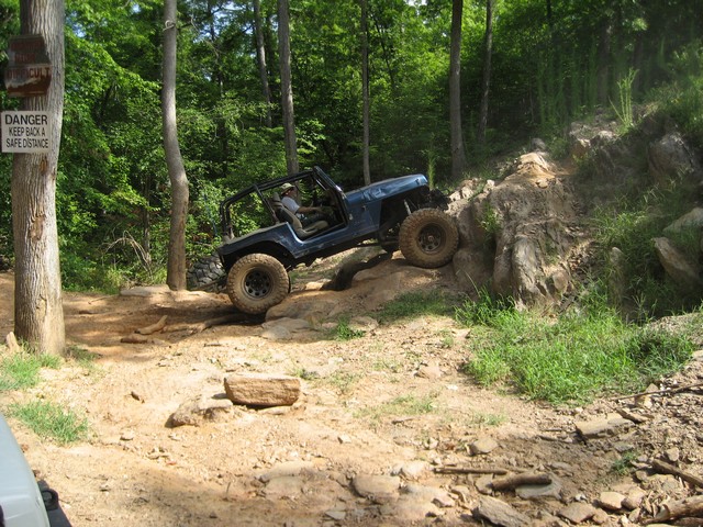 blue Jeep Wrangler climbing rocky trail, driver visible