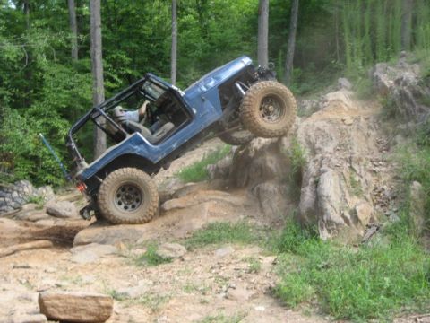 1995 Ford Bronco - Jeep Wrangler navigating a difficult rocky obstacle on an off-road trail.