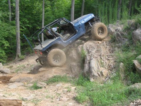 1995 Ford Bronco - A blue Jeep Wrangler navigates a challenging rocky incline on an off-road trail.