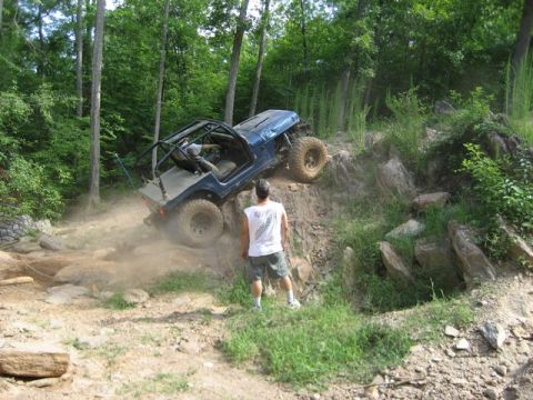 1995 Ford Bronco - An off-road vehicle navigates a challenging dirt trail surrounded by trees.