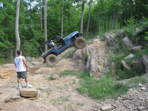 1995 Ford Bronco - A blue off-road vehicle navigates a challenging rocky terrain with a spectator observing the action.