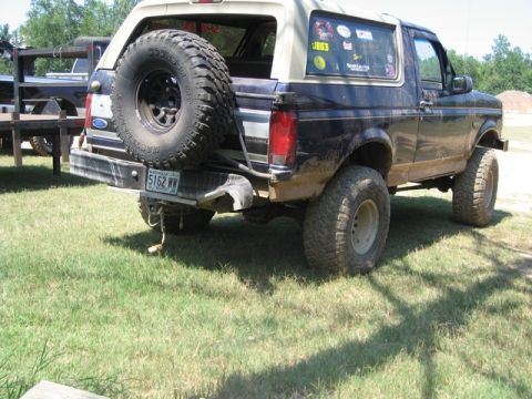 1995 Ford Bronco - This lifted Ford Bronco has a spare tire mounted on the rear bumper and is parked on grass next to another vehicle.