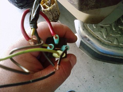 1986 Ford Bronco - A hand holds a wiring harness connected to a component, with a portion of a vehicle's bumper in the background.