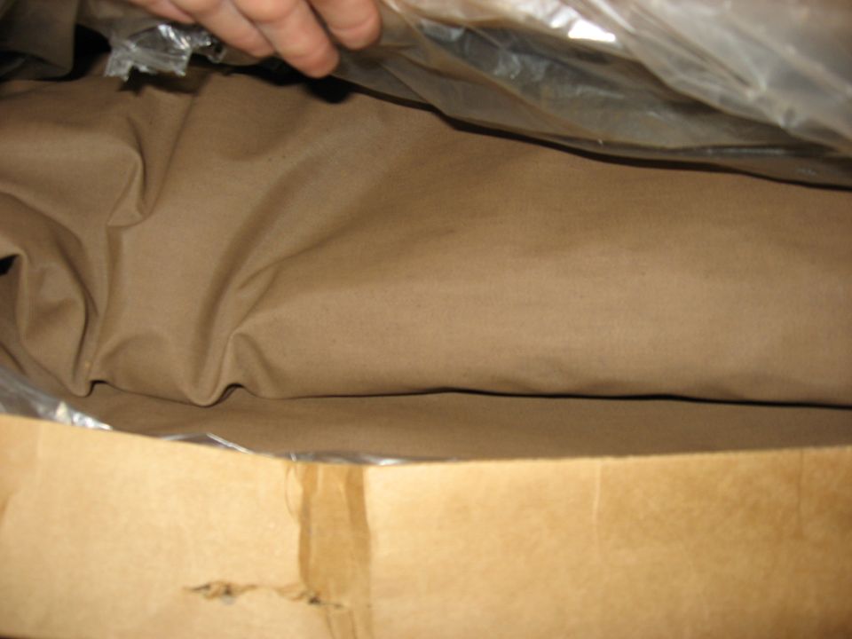 Folded tan soft-top fabric in plastic wrap inside an opened cardboard shipping box