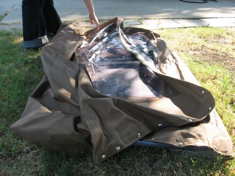 1989 Ford Bronco - A brown soft top with clear plastic windows is laid out on the grass, with a person's legs visible in the background.