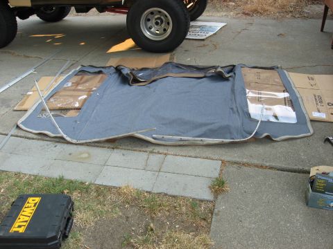 1989 Ford Bronco - A disassembled soft top is laid out on the ground next to a vehicle's tires and frame.