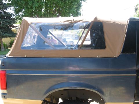 1989 Ford Bronco - Close side view of a tan canvas soft top newly fitted to the rear of a dark blue Bronco-style SUV, snapped down along the beltline with cle…