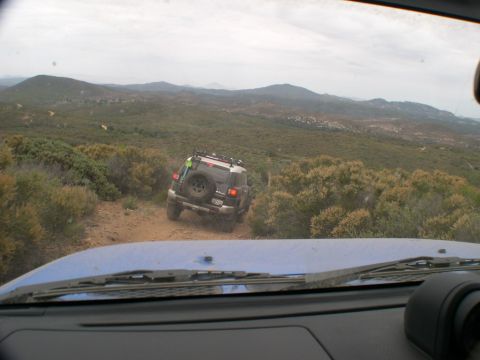 2007 Toyota FJ Cruiser - Two vehicles navigate a dusty trail through a hilly, overgrown landscape under a cloudy sky.