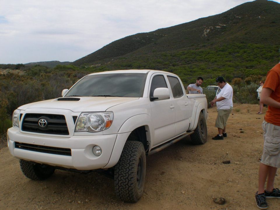 White Toyota Tacoma pickup truck, 3/4 front view. Hood scoop and off-road tires visible