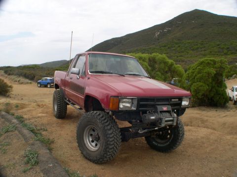 2007 Toyota FJ Cruiser - Modified red Toyota pickup truck on a dirt trail with a blue SUV in the distance.