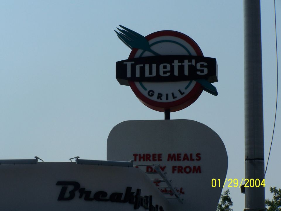 Truett's Grill sign with a fork and knife, "THREE MEALS DAY FROM" text, and "Breakfast" text on a building below