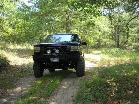 1995 Ford Bronco - This 1995 Ford Bronco is parked on a dirt path surrounded by trees.