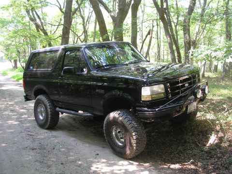 1995 Ford Bronco - A black Ford Bronco is parked on a dirt path surrounded by trees, its off-road capabilities.