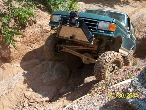 1979 Ford F-150 - A modified green truck tackles a challenging off-road trail with large tires and suspension.