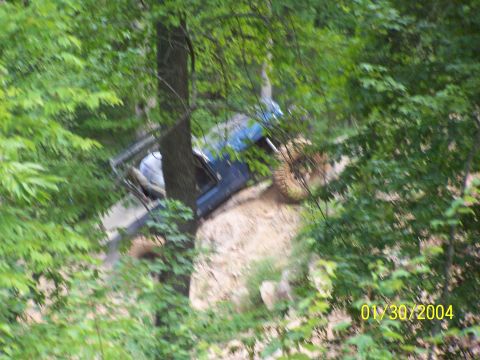 1979 Ford F-150 - A blue off-road vehicle navigates a steep dirt path amidst dense foliage.