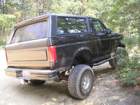 1995 Ford Bronco - Black 1995 Ford Bronco with aftermarket wheels and side steps on a wooded trail.