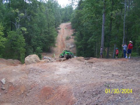 1979 Ford F-150 - A green off-road vehicle navigates a steep dirt path surrounded by trees.