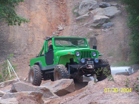 1979 Ford F-150 - A bright green Jeep tackles a challenging off-road course, with another vehicle partially obscured in the background.