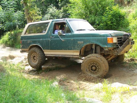 1979 Ford F-150 - A green Ford Bronco navigates a muddy off-road trail, its front tire partially submerged in the muck.