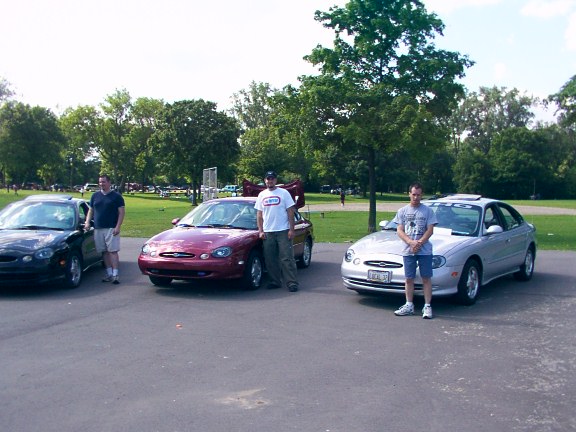 Three Ford Taurus sedans parked in a lot with people standing by them
