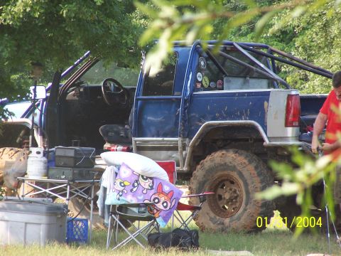 1979 Ford F-150 - A heavily modified blue pickup truck sits in a grassy area, showing its off-road tires and custom roll cage.