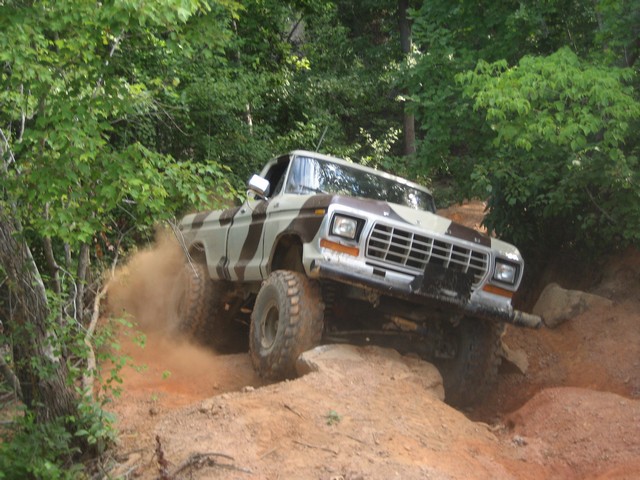 Camouflaged 1979 Ford F-150 climbing a dirt hill, kicking up dust