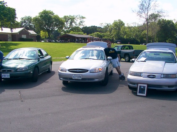 1998 Ford Taurus, silver, 3q-front view. Man leaning on car