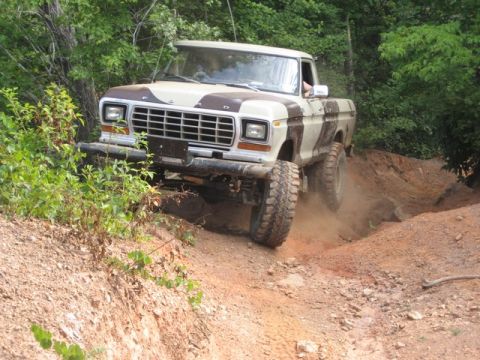 1979 Ford F-150 - A lifted Ford pickup truck navigates a steep, dusty trail surrounded by trees.
