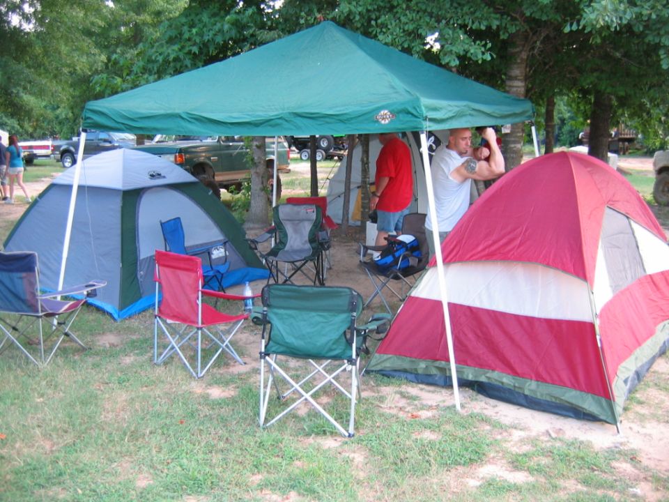 Campsite with two tents, canopy, chairs, and people standing