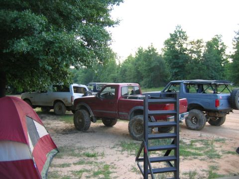 1992 Ford Mustang - A group of off-road vehicles are parked together in a wooded area, with a tent set up nearby.